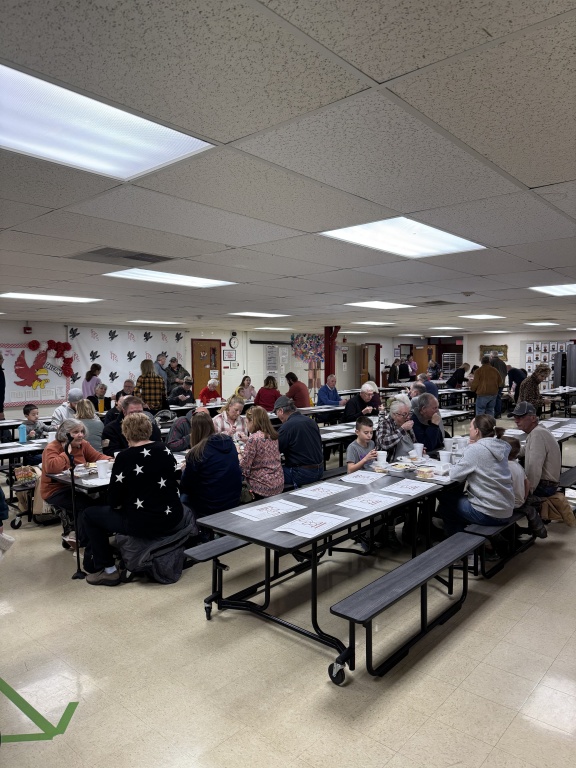 Crowd gathered in the cafeteria enjoying their meals.